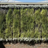 Painel de jardim vertical instalado em parede de tijolos, com plantas cobrindo toda a superfície