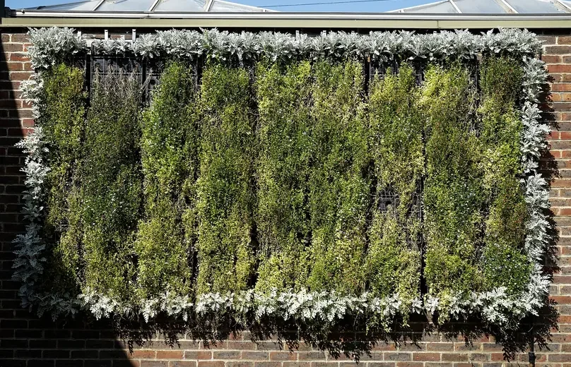 Painel de jardim vertical instalado em parede de tijolos, com plantas cobrindo toda a superfície