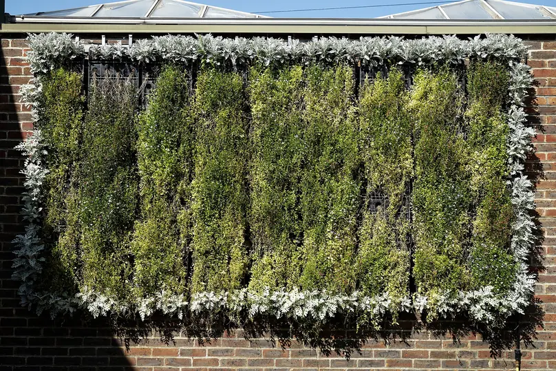 Painel de jardim vertical instalado em parede de tijolos, com plantas cobrindo toda a superfície