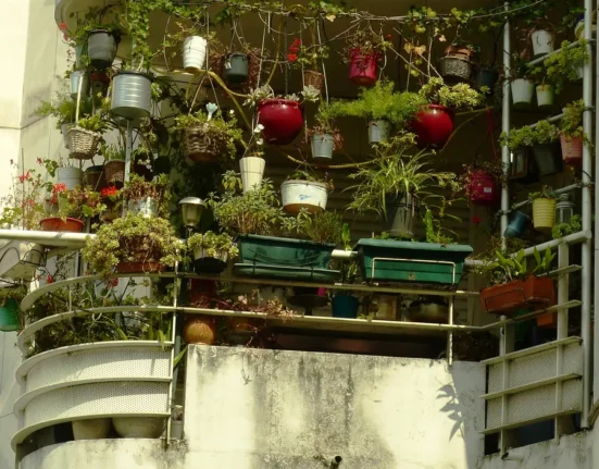 Varanda de apartamento tomada por vasos pendurados, em grades e em jardineiras