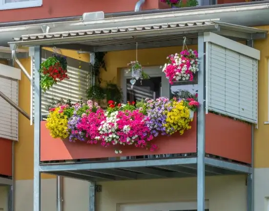Varanda de apartamento ensolarada com floreira e cestos suspensos repletos de petúnias, calibrachoas e gerânios floridos